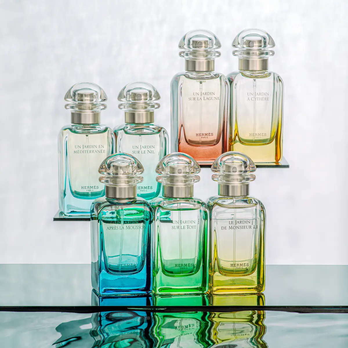 Reklamná fotografia parfumov Hermès Un Jardin – sklenené flakóny, odraz vo vode a luxusná kompozícia